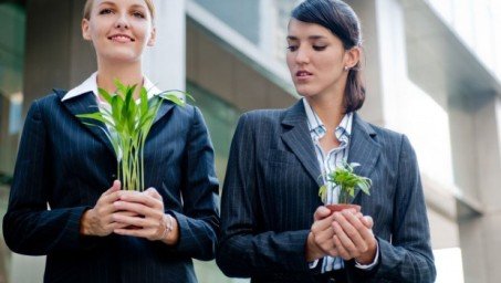 Two women in pantsuit holding plants