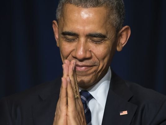 Obama holds hands in prayer with eyes closed and a smile