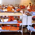 Prison inmates sit or lay in their bunkers wearing orange jumpsuits