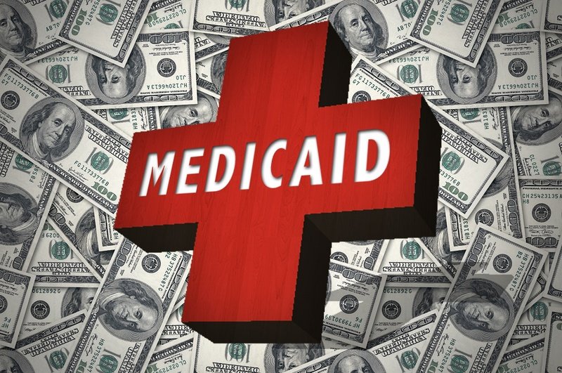Red cross reads Medicaid and embossed on top of a pile of 100 dollar bills