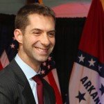 Tom Cotton smiles at camera with flags in background