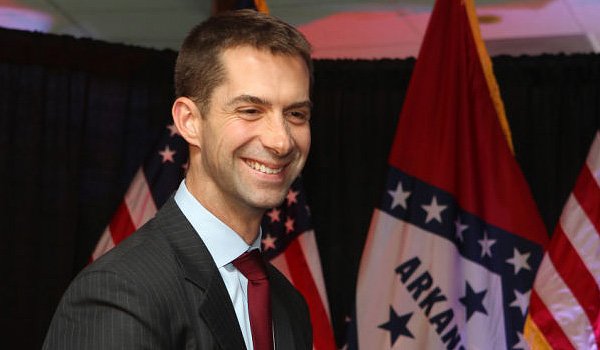 Tom Cotton smiles at camera with flags in background