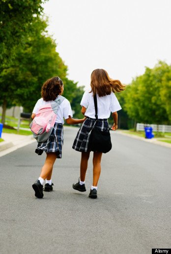 Rear view of two school girls walking down street holding hands