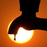 Droplet of water from a faucet with bright sun in background