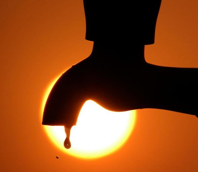 Droplet of water from a faucet with bright sun in background