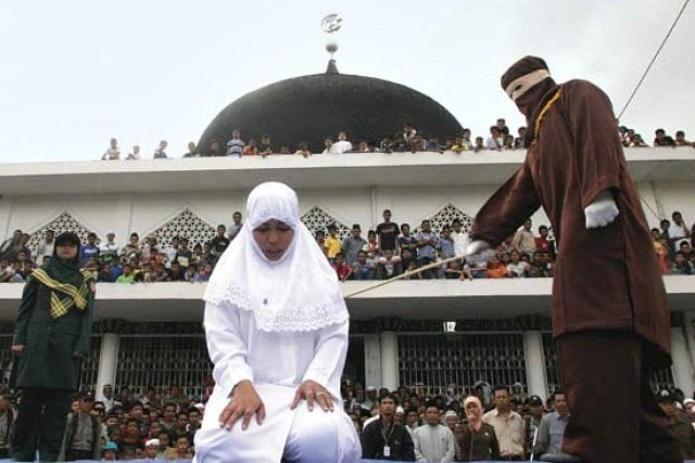 Woman in white hijab is canned by masked person by form of punishment