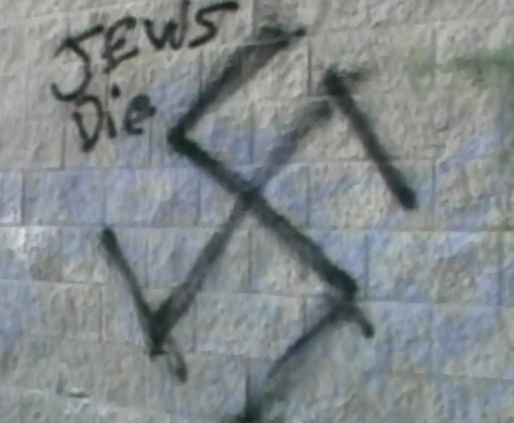 Nazi symbol graffiti on stone wall with words Jews Die