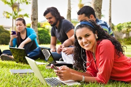 Four young adults sit on grass with computers and smartphones