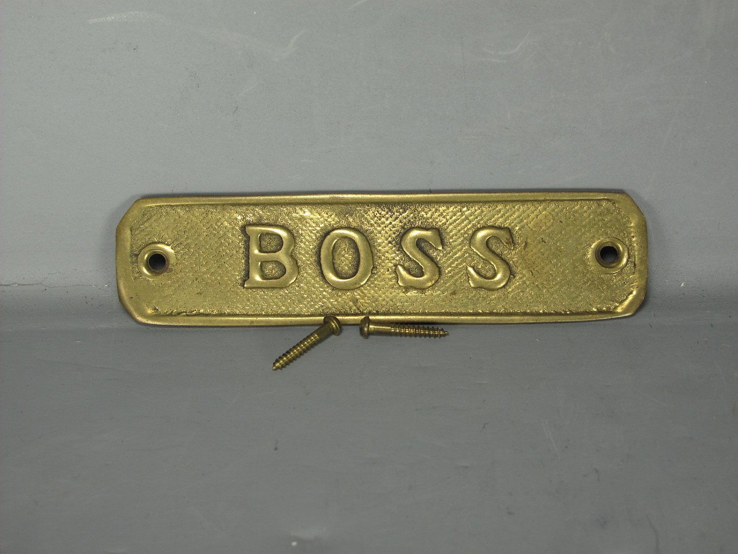 Gold plated sign reads BOSS with screws sitting in front of sign