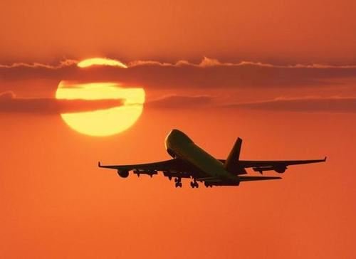 Airplane flying off toward orange sunset filled sky