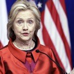 Hillary Clinton in red attire gives speech with serious facial expression