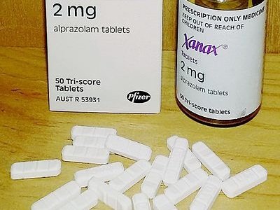 Bottle of Xanax on wooden table surrounded by white pills