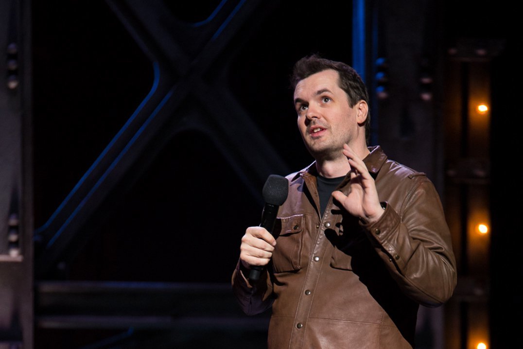 Comedian Jim Jeffries in brown leather coat performs live
