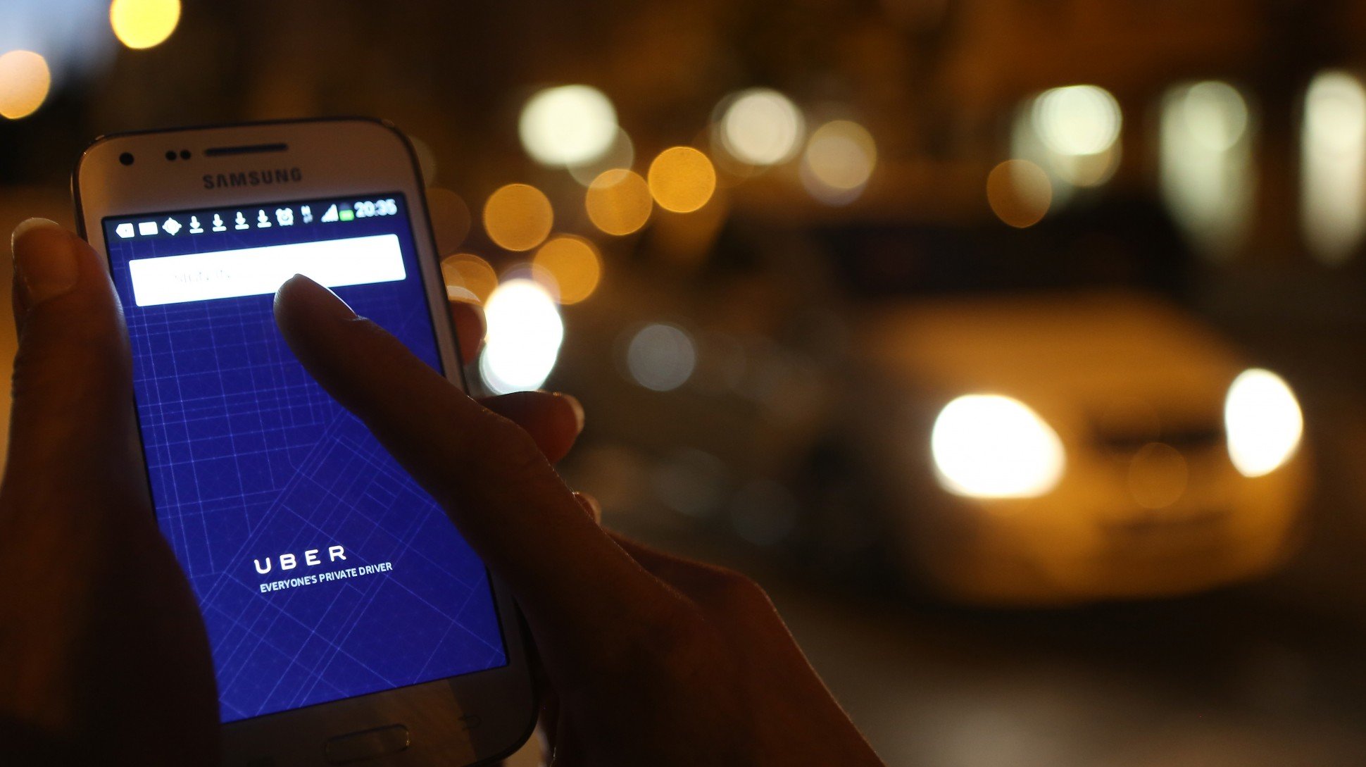 Woman using Uber private driver app with city lights in background