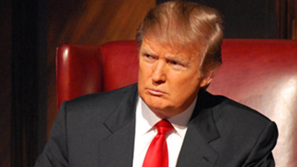 Donald Trump sitting in a red chair with a red tie