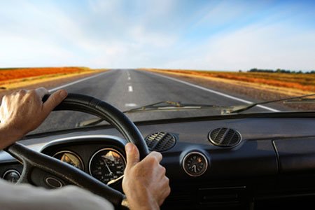 Man behind steering wheel driving on long road