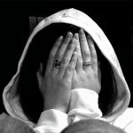 Woman wearing hooded sweater hides face behind hands